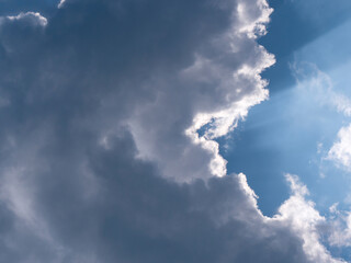 Fototapeta na wymiar Cloudscape with sunrays peeking over the edge of majestic gray cumulus cloud