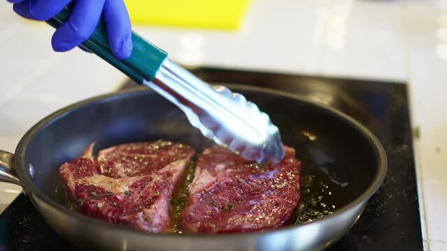 in a hot frying pan fry pieces of meat with garlic and rosemary. cooking steaks.