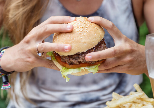 Hands holding a burger, on a restaurant table. Delicious and nutritious food.