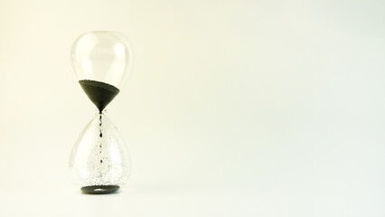 Hourglass on a white background. Black sand flows down the transparent glass. copy space.