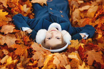 Little girl smiles lying in orange autumn fallen maple leaves 