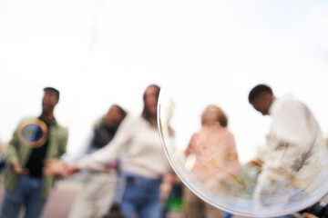 Focus on a soap bubble. Defocus in the background Happy people dancing outdoors. Group of friends having fun in a day party.