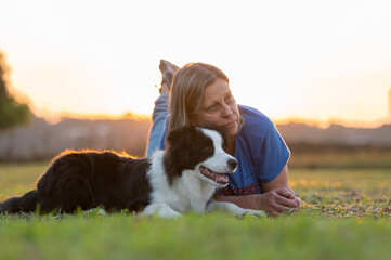 Woman and Border Collie dog lying on the grass in the park during golden hour.