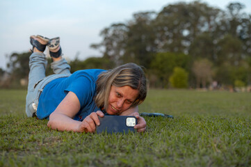 Woman lying on the grass taking a picture with cellphone in the park during the day