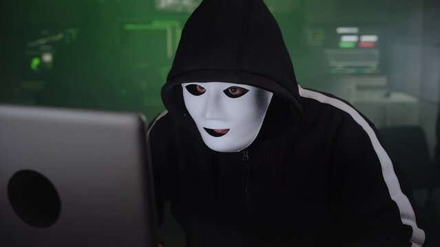 Masked Hacker is Using Computer for Organizing Massive Data Breach Attack on Corporate Servers. They're in Underground Secret Location Surrounded by Displays