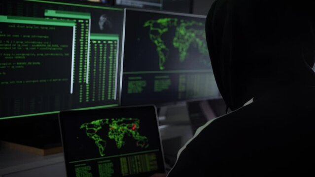 Criminal team Hacker using computer for organizing massive data breach attack on government and big company servers. Dark room surrounded computers