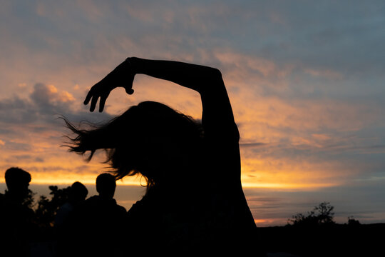 Summer sunset scene.  Woman silhouette posing with people and orange sunset in the background.