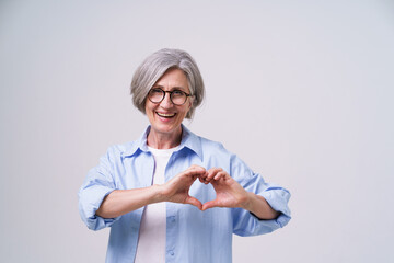 Gesturing love, heart with hands happy mature grey hair woman in studio. Senior woman gesturing...