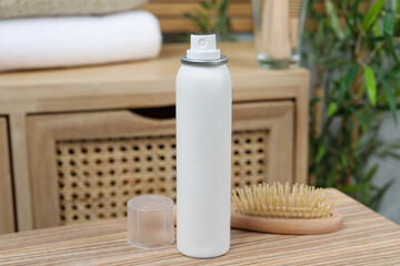 Fototapeta na wymiar Dry shampoo spray and hairbrush on wooden table in bathroom