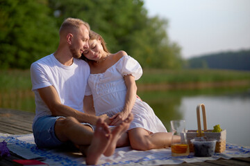 A couple in love are having a picnic in nature by the lake. Hugging, kissing, having a good time. The concept of a happy family.