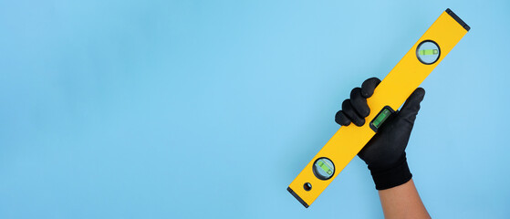 Hand wearing black gloves holding yellow black water level isolated baby blue background with copy space