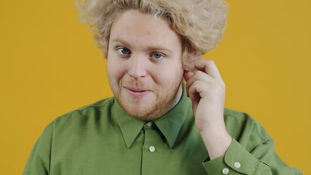 Portrait of young man wearing earpods looking at camera and showing thumbs-up hand gesture on yellow background. Modern devices and youth concept.