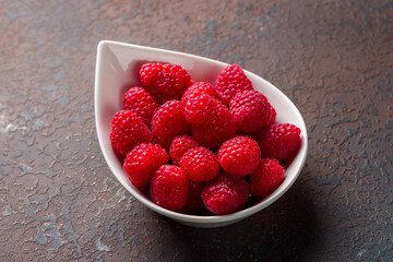 Fresh raspberry on white plate on dark stone table macro close up
