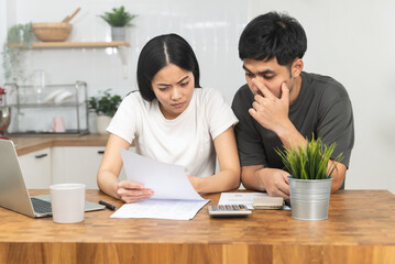 Stressed Asian couple looking at financial debt notice papers from bank.