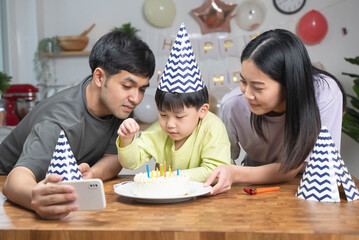 Asian family blowing birthday cake in living room
