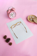 Cat's eye glasses in the photo from above with a minimalist concept on a purple paper background with an alarm clock decoration and dry leaves