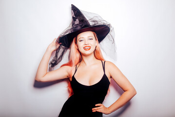 Pink-haired woman witch, in a hat on a white background, halloween costume. The girl smiles and looks to the side at the empty space. Halloween party.