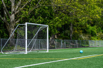Blue soccer ball on an artificial turf field and white netted goal on a sunny spring day
