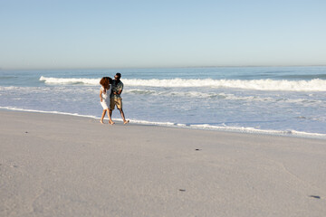 A mixed race couple walking and laughing on beach on a sunny day