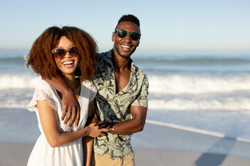 A mixed race couple laughing and looking into the camera on beach on a sunny day