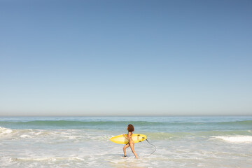 Mixed race woman holding surf board on the beach