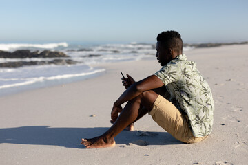 African american man using his phone on the beach