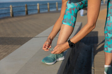 Female jogger tying her shoe laces on seaside