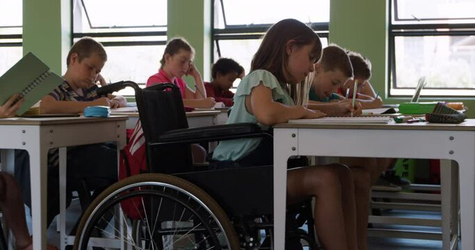 Physically challenged girl writing in her notebook in the class