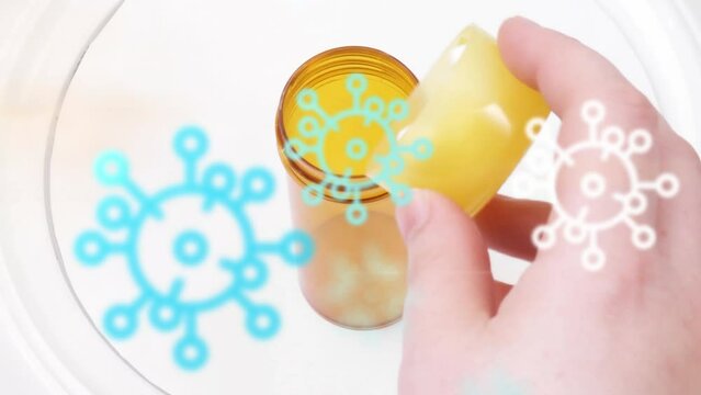 Animation of floating Covid-19 cell icons over Caucasian hand pouring pills in a box