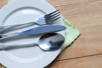 Fork, spoon, and knife stainless steel in empty white plate, place on wipe isolated on wooden background closeup.