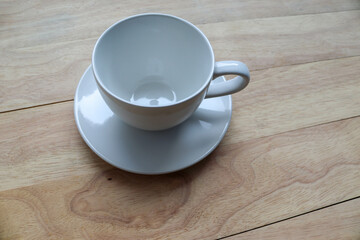 Empty white coffee cup with plate isolated on wooden background closeup.
