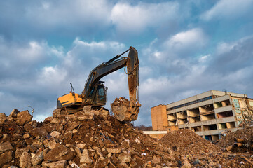 Bucket of excavator digs leftovers of destroyed building