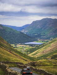 Vertical view of mountains and distant lake in English Lake District at the end of summer; road with stone wall  and car in foreground