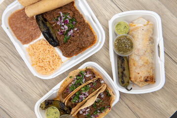 Overhead view of Mexican food feast on the table with choices of burrito, birria stew meat combo, or 3 tacos served with guacamole, salsa, and a grilled jalapeno