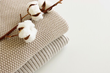 Beige knitted blankets stack and cotton flowers on white  background with copy space.Autumn, winter  concept.Flat lay, top view