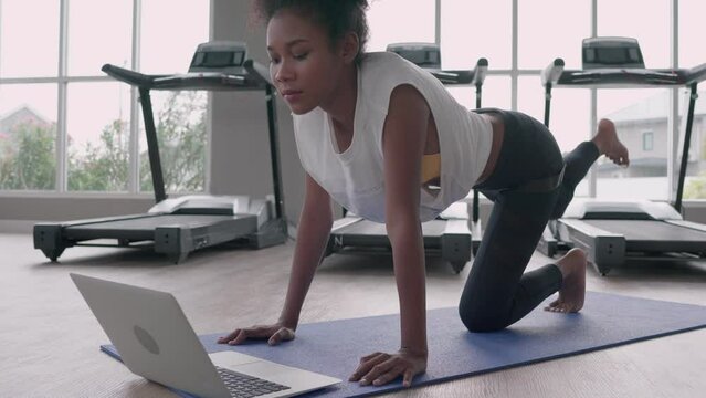 Fitness young black woman doing exercise yoga in gym. African american female loook at laptop computer lesson practicing Yaga plank pose on social online internet class. Healthy lifestyle concept.