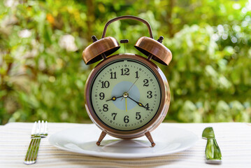 Diet / weight loss or time to eat concept : Vintage or classic alarm clock on a white plate or dish...