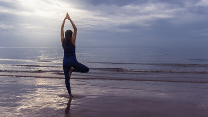 Fototapeta na wymiar Asian woman warm up and play yoga exercise on the beach by the sea at morning sky background.