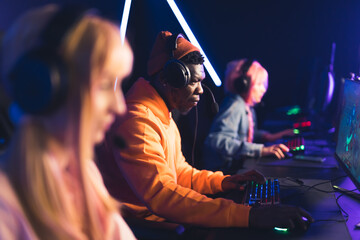 Three teenagers wearing colorful clothes focused on playing online game tournament together using professional gaming setup. Blue lighting. Horizontal shot. High quality photo