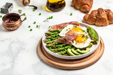 Tasty breakfast. avocado, asparagus, jamon, ham, prosciutto and fried egg on white plate. Ketogenic...