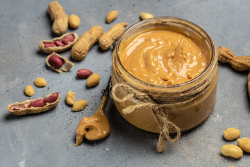 Fototapeta na wymiar Peanut butter or paste in an open jar and peanuts in the peel scattered on a light background, banner, menu, recipe place for text, top view