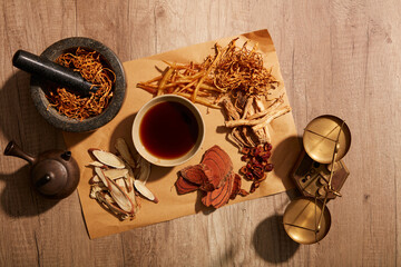 The mortar containing the cordyceps and herbs around the teacup on a wooden background