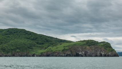 The picturesque coast of Kamchatka against the background of cloudy sky and ocean.  Green hills and steep cliffs. Avacha Bay