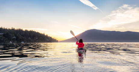 Adventurous Woman on Sea Kayak paddling in the Pacific Ocean. Sunny Summer Sunset. Taken near...