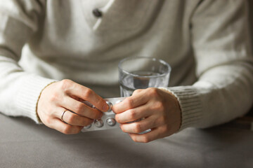 Obraz na płótnie Canvas Man's hands holds and open silver blister with pills, and ready to take medicines with glass of water. Health care.