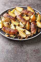 Roast beef rolls with baked potato wedges and mushrooms served on plate closeup on the table. Vertical