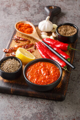 Harissa Paste North African spicy red sauce to add heat to dressings, sauces, soups in bowl on wooden board with ingredients closeup. Vertical