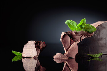 Large piece of dark bitter chocolate with mint on a black reflective background. - obrazy, fototapety, plakaty