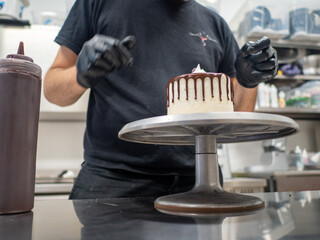 cake designer decorating a chocolate drip cake with mering and blueberries