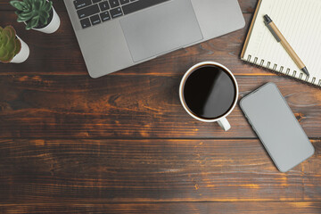 Top view desk of work office with laptop, smartphones, a pen, green leaf, and coffee of cup on old wooden background with copy space. Flat lay, top view. Old wood office table.